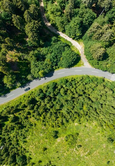 Luftaufnahme der Straße mit Wald und schwarzes Auto | © villacher-alpenstrasse.at/Stabentheiner