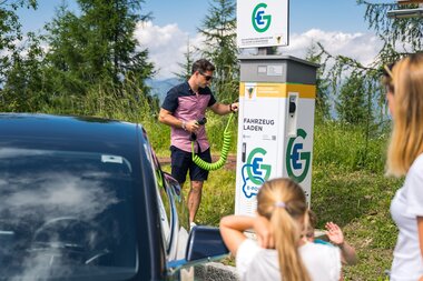 Mann neben E-Tankstelle und E-Fahrzeug | © villacher-alpenstrasse.at/Stabentheiner